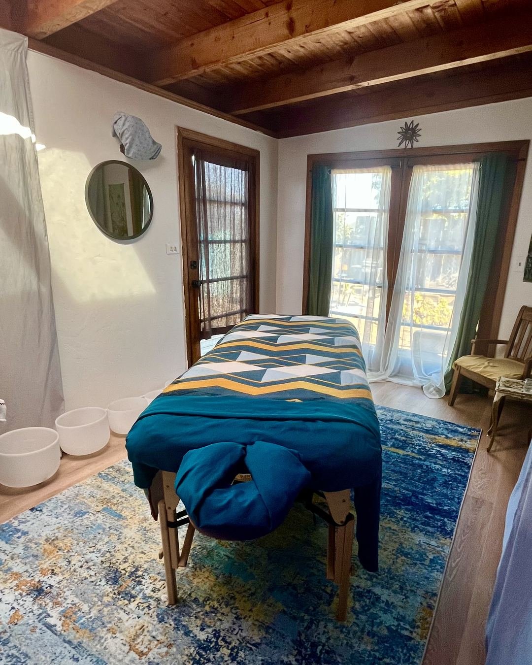 Treatment room with a massage table, crystal singing bowls and a blue rug